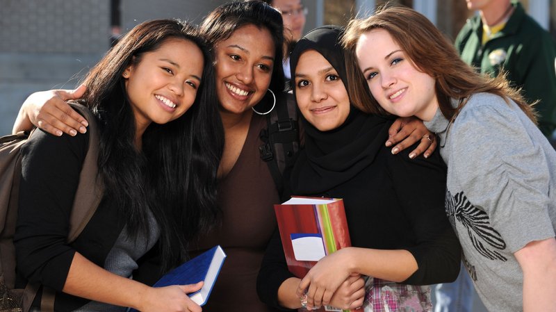 Vier junge Studentinnen umarmen sich und blicken in die Kamera.